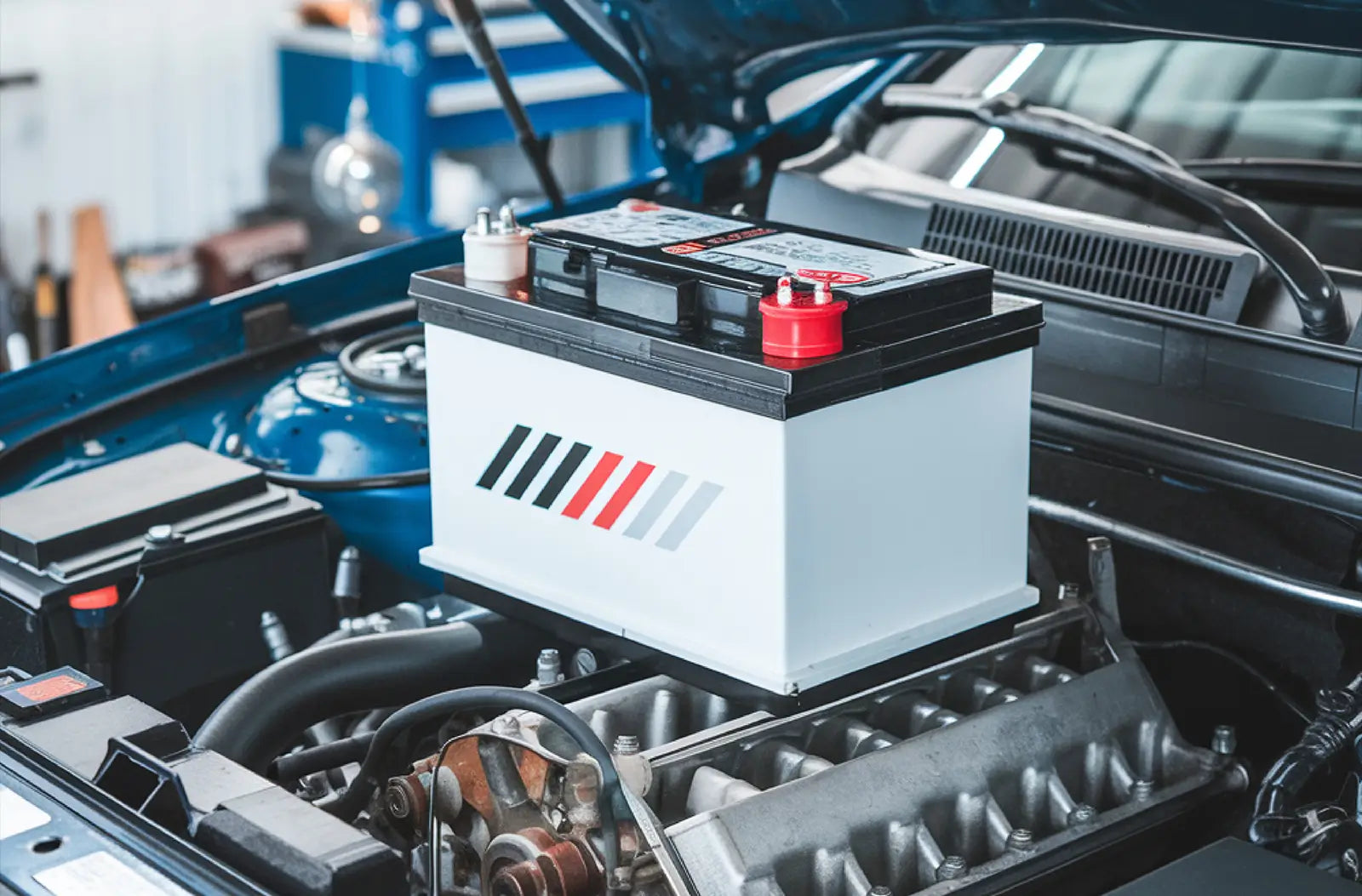 Shows a clean, new white car battery with red and black terminal covers installed inside an open vehicle engine bay.