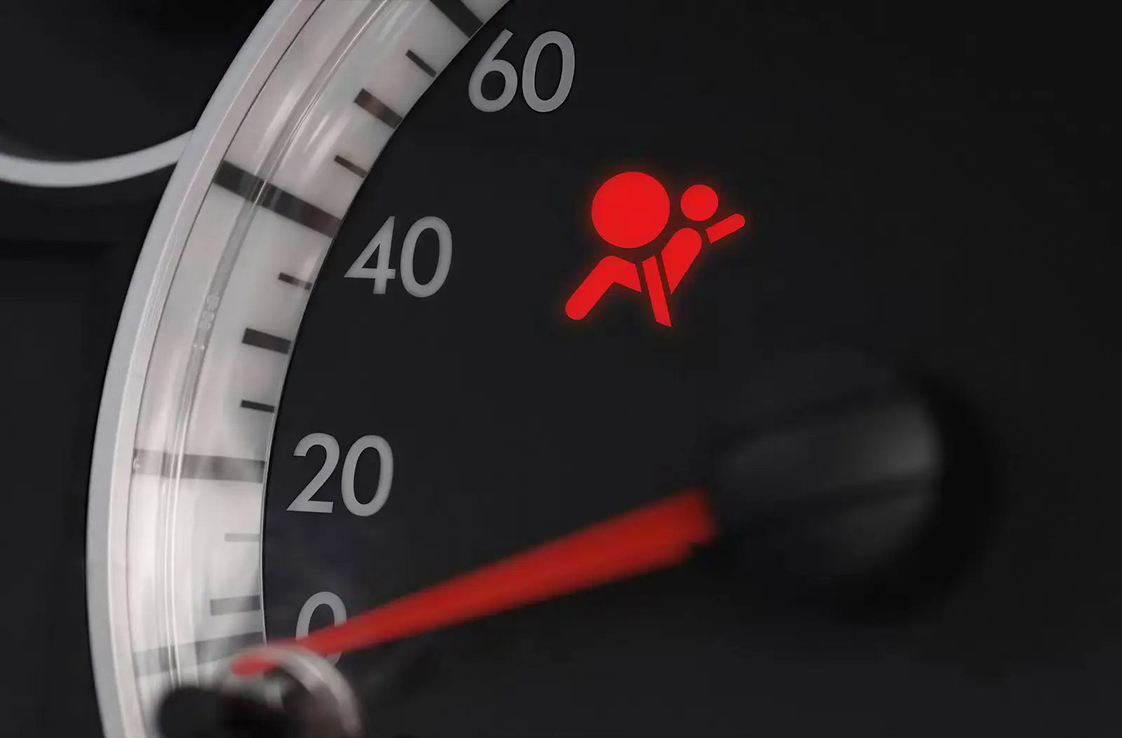 Close-up of an analog vehicle gauge cluster with a prominent red "Airbag / SRS" passenger safety warning symbol illuminated.