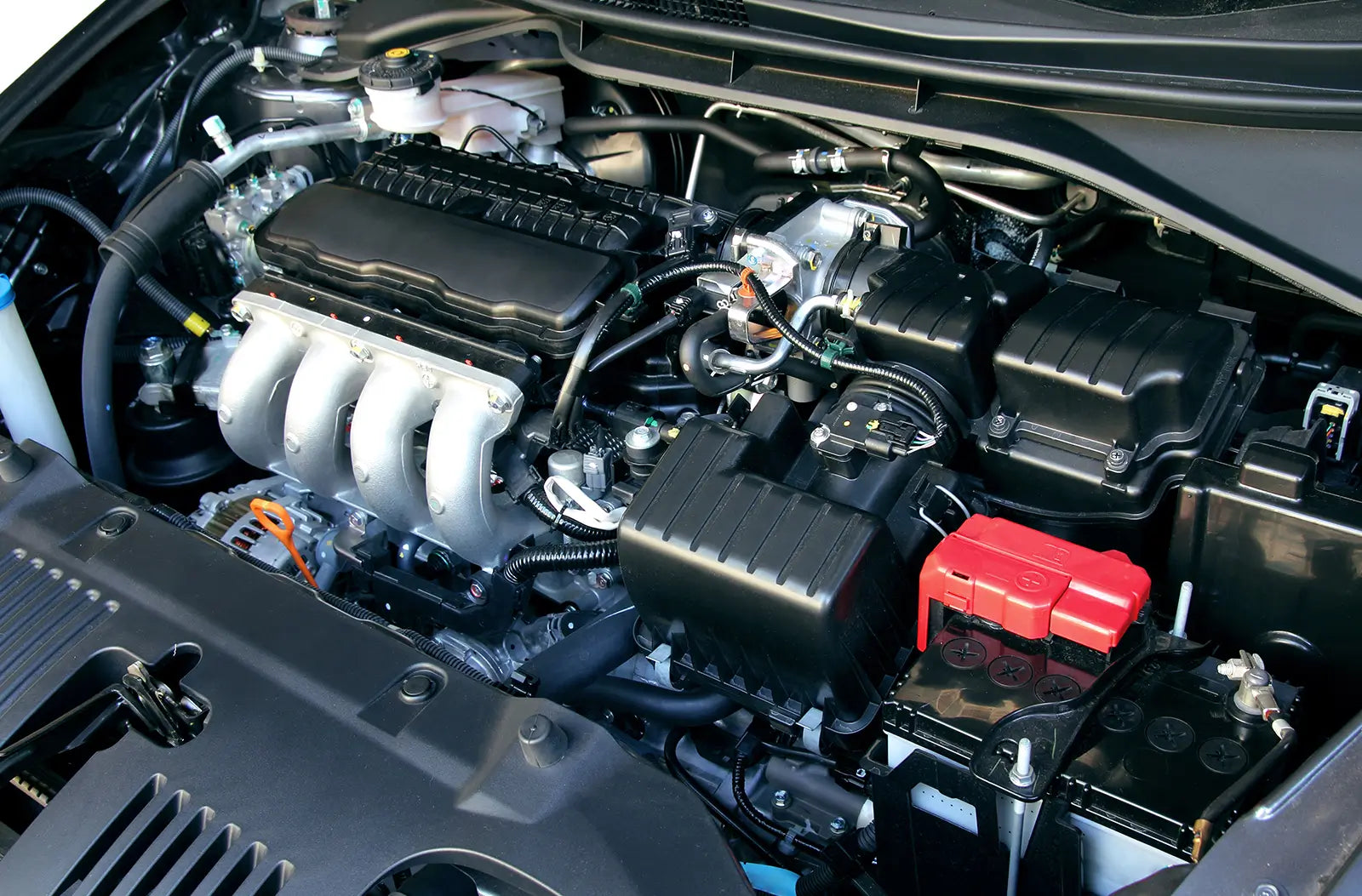 Shows a modern car engine bay with the plastic cover removed, revealing the ignition coils, spark plug wires, and top-end component layout.