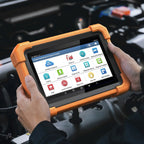 a person's hands holding a LAUNCH Creader Professional 919 Expert diagnostic tablet over an open car engine bay. The device is enclosed in a rugged orange protective bumper and features a touchscreen displaying various automotive diagnostic menu icons.